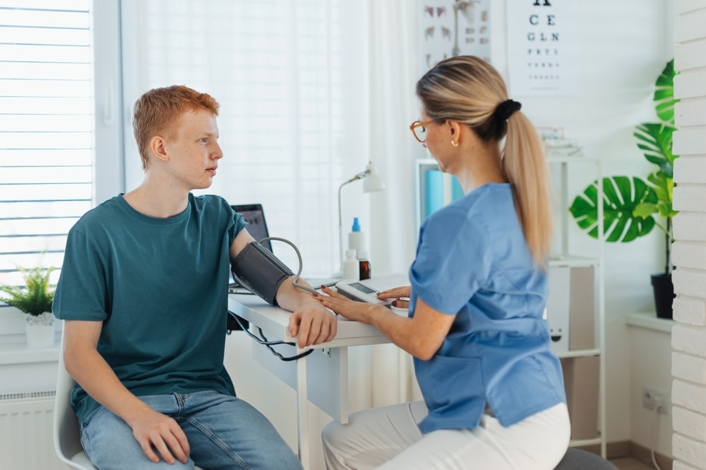Doctor measuring teenage boy’s blood pressure during annual preventive physical exam, highlighting adolescent health care and college physical requirements.