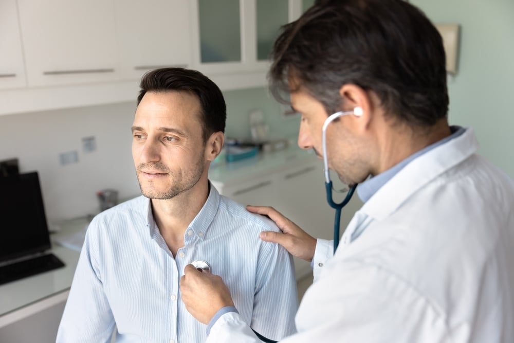 A cardiologist conducts a thorough clinical examination by using a stethoscope to assess a male patient’s heart and lung function during a general check-up.